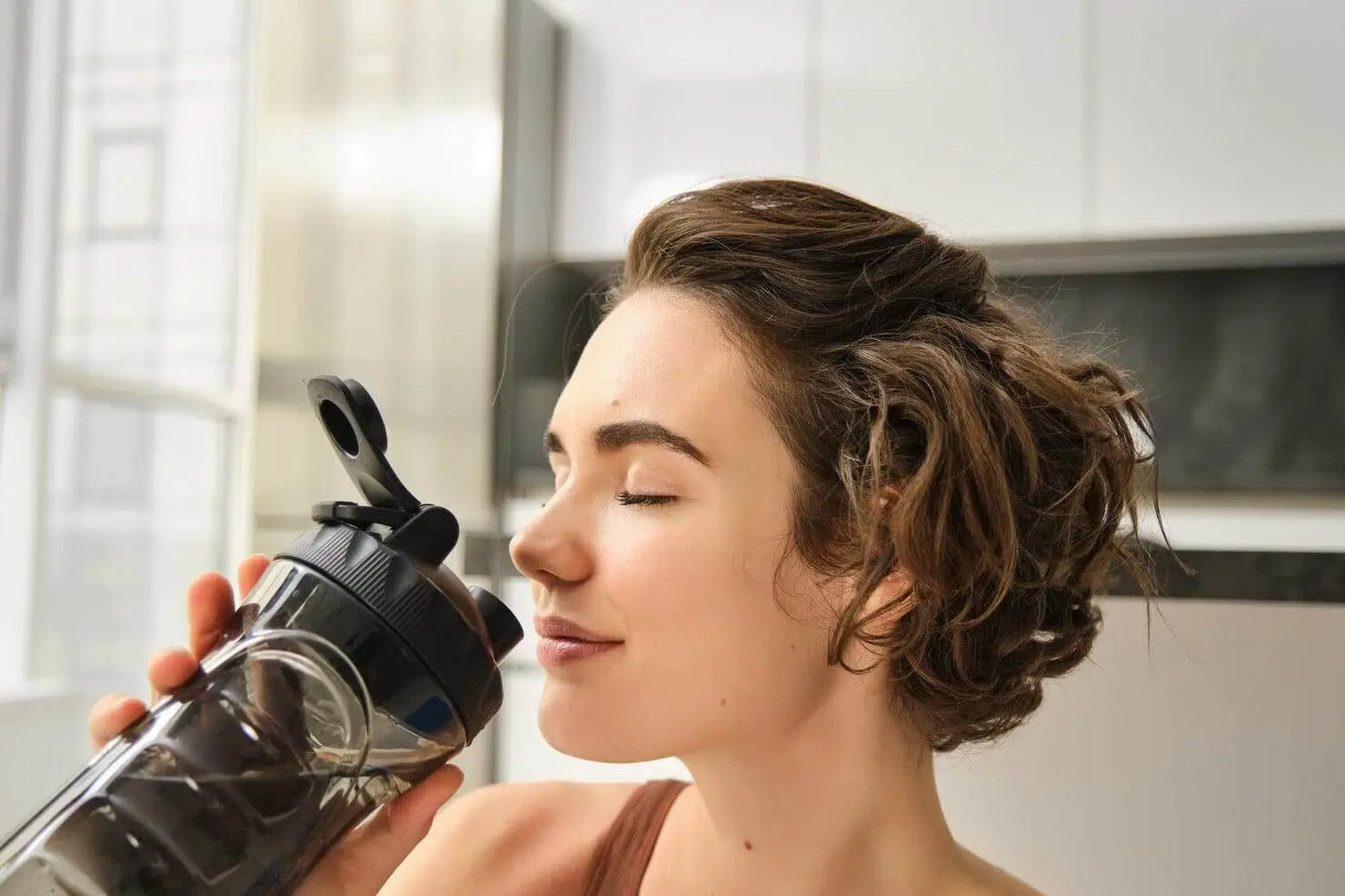 woman with eyes closed drinking from water bottle image