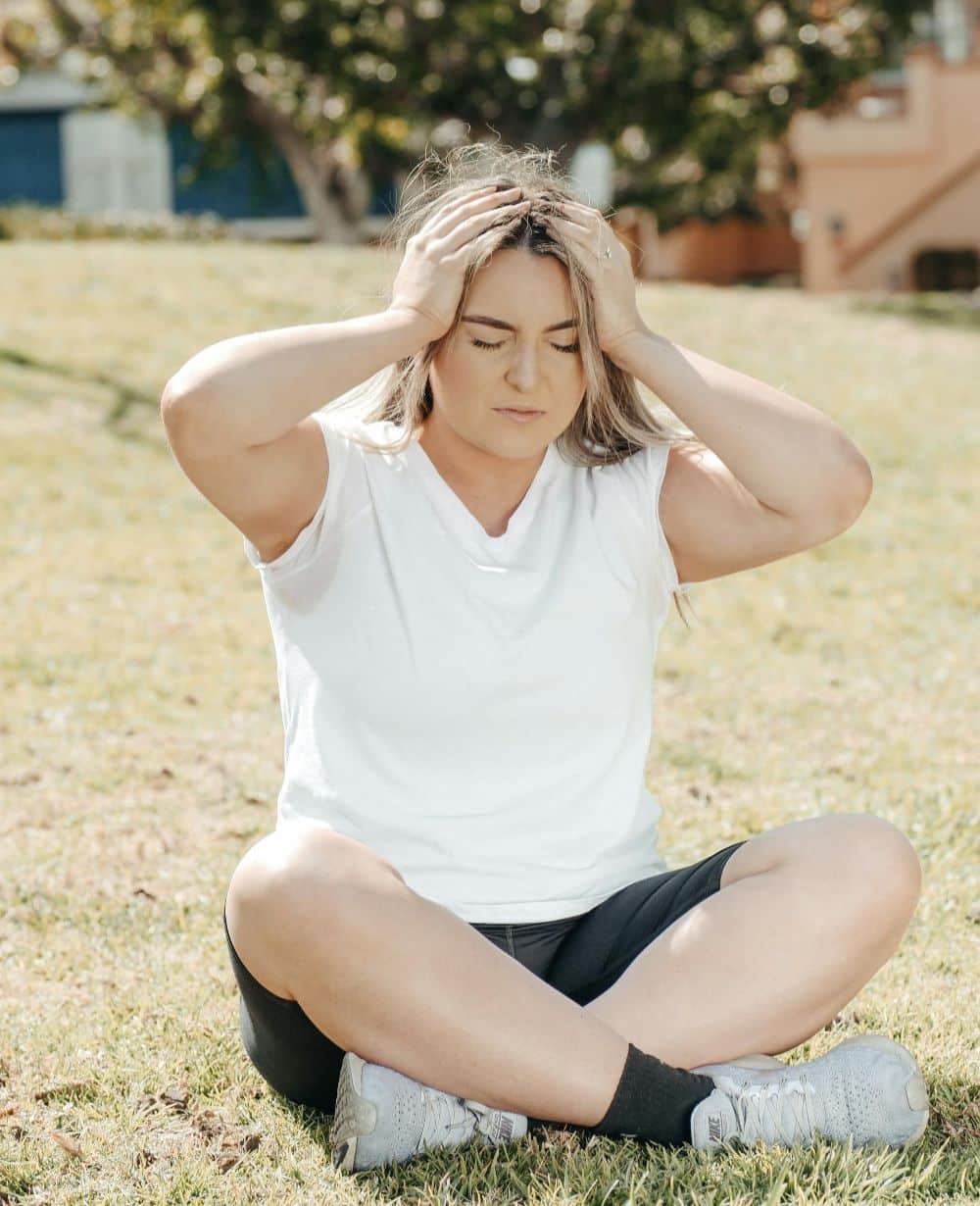 woman sitting on ground with two hands on sides of head image